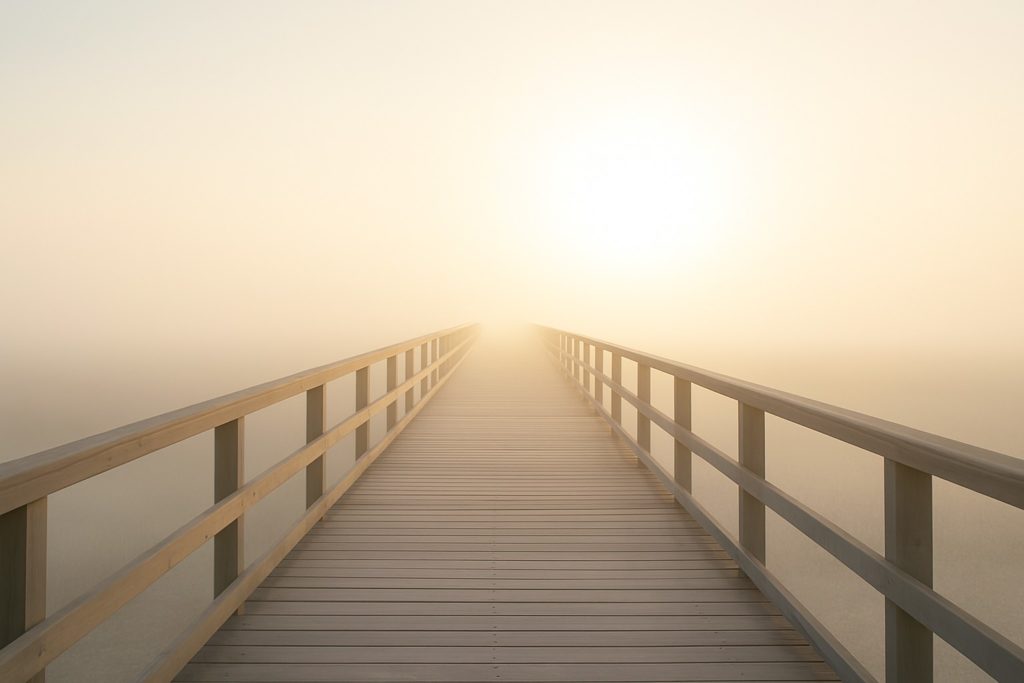 Heller Holzsteg im Nebel mit sanftem Sonnenlicht am Horizont